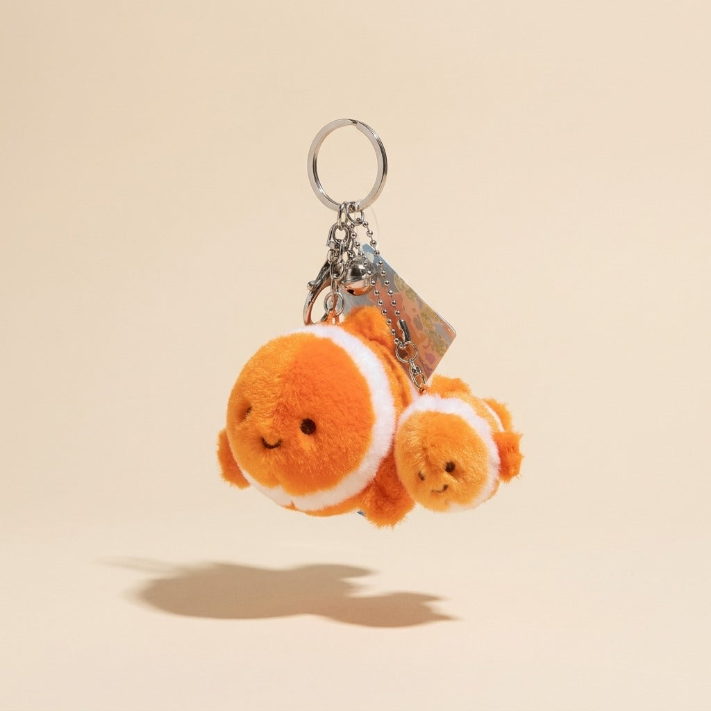 A plush keychain featuring two orange and white clownfish characters with a silver metal key ring and keychain hardware, shown against a solid beige background.