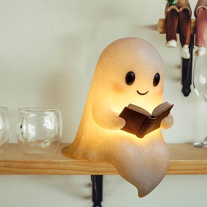 A 3D-printed silicone ghost reading lamp sitting on a shelf with a warm LED glow.
