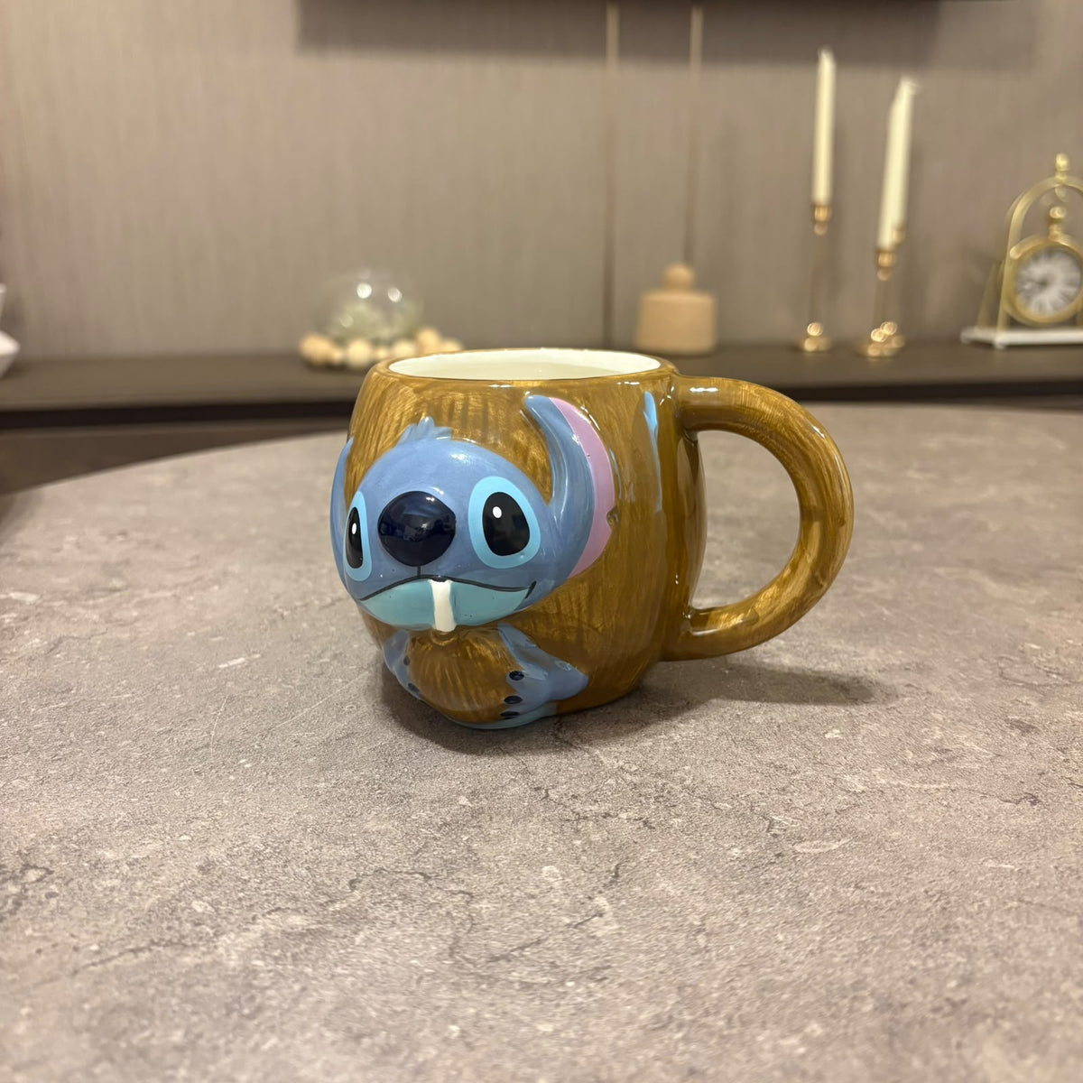 A ceramic mug shaped like a blue cartoon character with a brown body, placed on a gray stone surface in a softly lit indoor setting.
