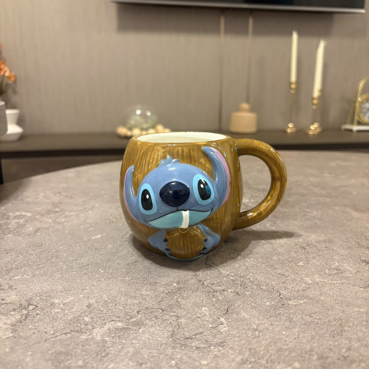 A ceramic mug featuring a detailed 3D character design resembling Stitch, sitting on a gray stone countertop in a kitchen setting.