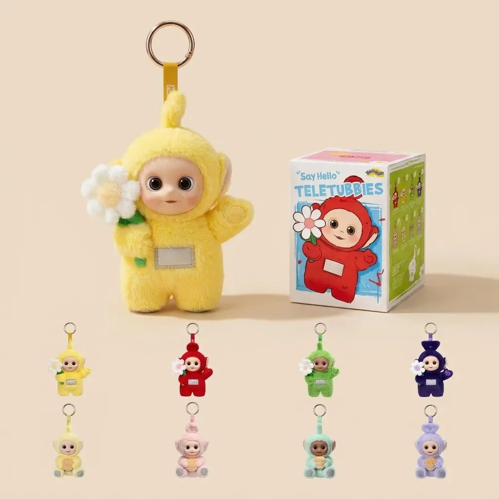 A yellow Teletubbies character plush keychain holding a white flower stands next to its branded box on a warm beige background. Smaller versions of the same keychain in other colors are lined up along the bottom.