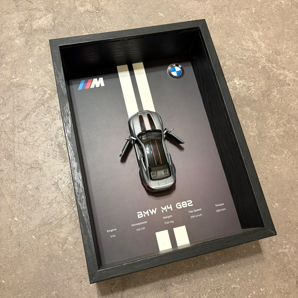 BMW M4 3D Framed Diecast Wall Art in a 32cm x 23cm black shadow box frame, featuring a grey 1:32 scale model car with open doors against an M-Power design background with performance stats.