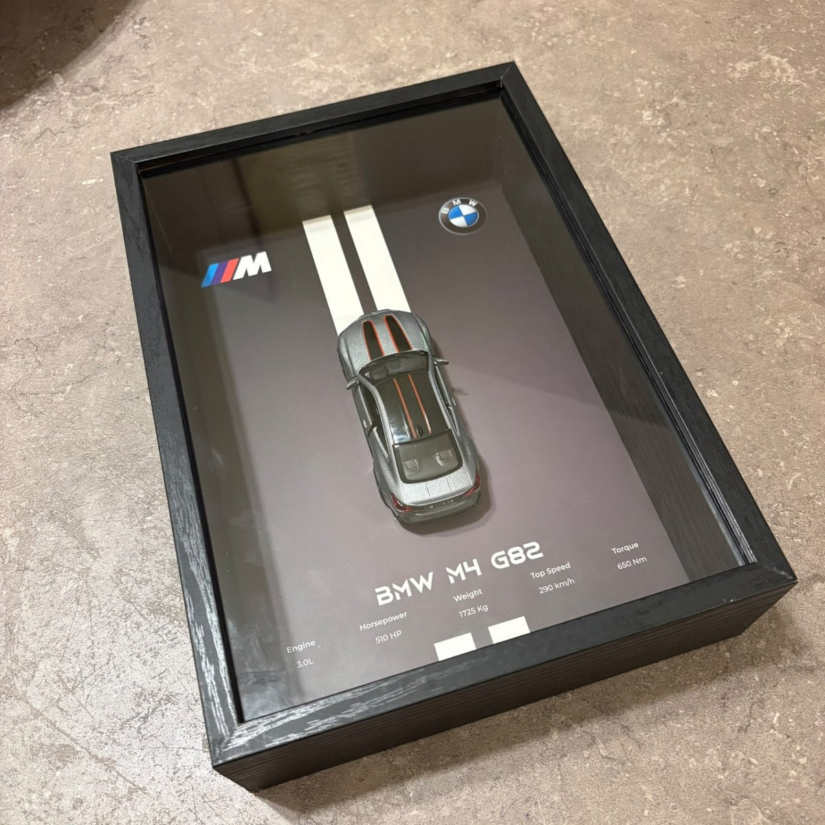 BMW M4 3D Framed Diecast Wall Art in a 32cm x 23cm black shadow box frame, featuring a grey 1:32 scale model car with open doors against an M-Power design background with performance stats.