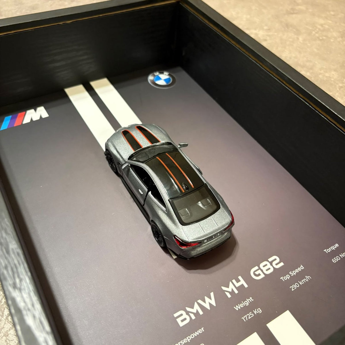 BMW M4 3D Framed Diecast Wall Art in a 32cm x 23cm black shadow box frame, featuring a grey 1:32 scale model car with open doors against an M-Power design background with performance stats.