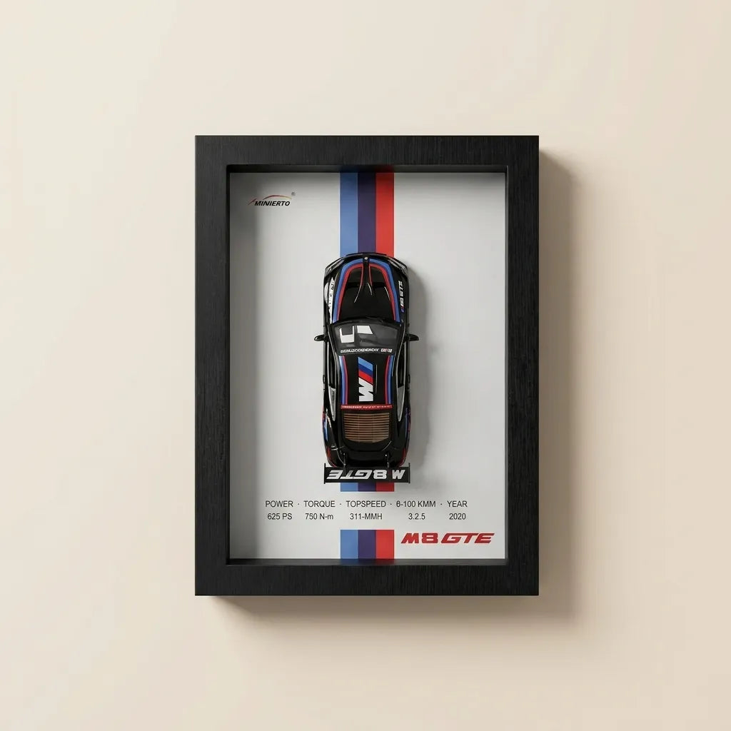 A framed automotive poster featuring a top-down view of a black BMW M2 GTE race car with red, white, and blue racing stripes, mounted on a light beige wall.