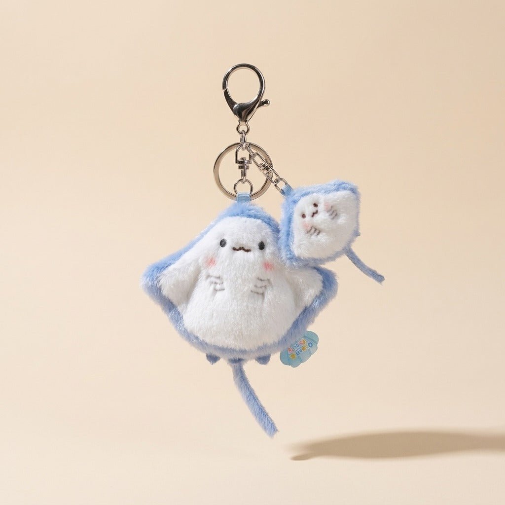 A cute plush keychain shaped like a white cloud with light blue stitched outlines and a small matching cloud charm, attached to a black metal clasp on a warm beige background.