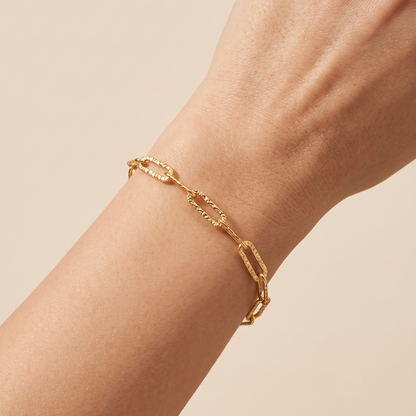 A close-up of a gold chain link bracelet worn on a person's wrist against a soft beige background.